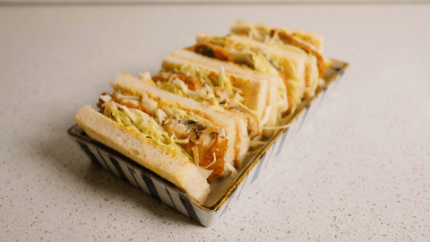 A horizontal stack of fried mackerel sandwiches in a rectangular dish.